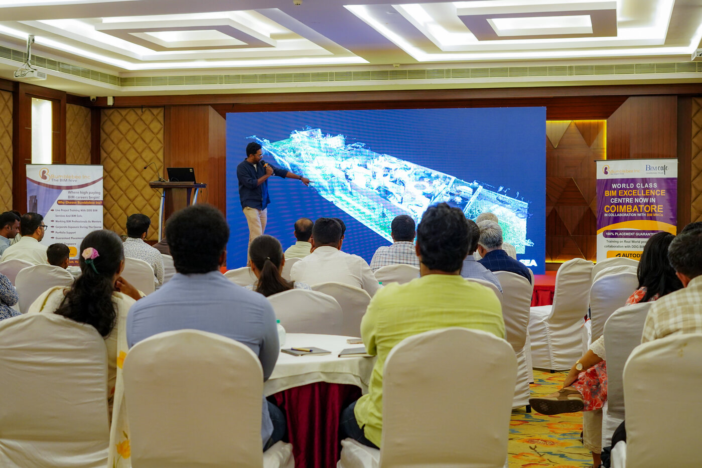 Participants at a Bumblebee Inc programme watching a point cloud scan of a long building on a large screen